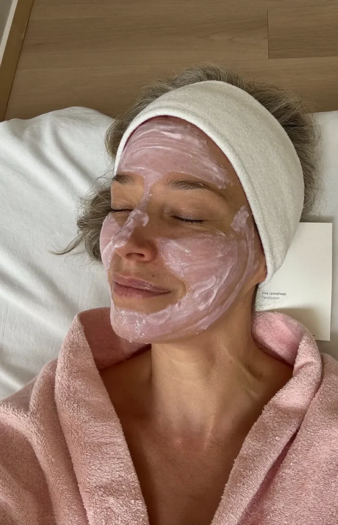Vrouw met een roze verzorgend masker en haarband ontspant met gesloten ogen